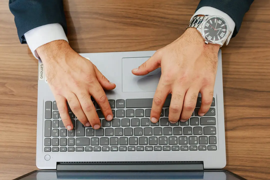 Manos escribiendo en una laptop sobre un escritorio